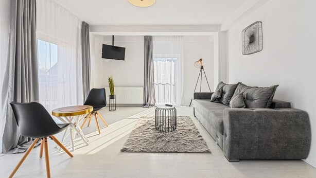 A modern living room with a grey sofa, black chairs, a round coffee table, and a TV mounted on the wall. - MoHost Harmony Apartments - City Center  (Brașov)