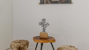 A room with a wall-mounted tapestry, a small wooden table with a vase, and two stool-like chairs. - MoHost Harmony Apartments - City Center  (Brașov)