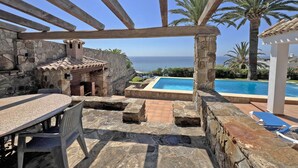 A stone patio with a pool, outdoor seating, and a view of the sea. - Charming rustic villa with sea views in Playa del Faro Camarinal (Tarifa)