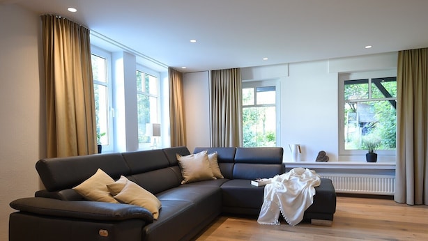 Un salón moderno con un sofá modular, ventanas amplias y un radiador.
