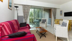 Ein Wohnzimmer mit einem roten Sofa, einem weißen Korbstuhl, einem kleinen Holztisch und einem an der Wand befestigten Fernseher.