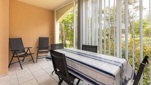 Ein Balkon mit Tisch und zwei Stühlen, Blick auf Bäume und ein Gebäude im Hintergrund.