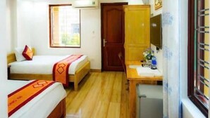 Une chambre d’hôtel de taille modeste, équipée de deux lits simples, d’un petit bureau, d’un ventilateur et d’une fenêtre avec des rideaux.