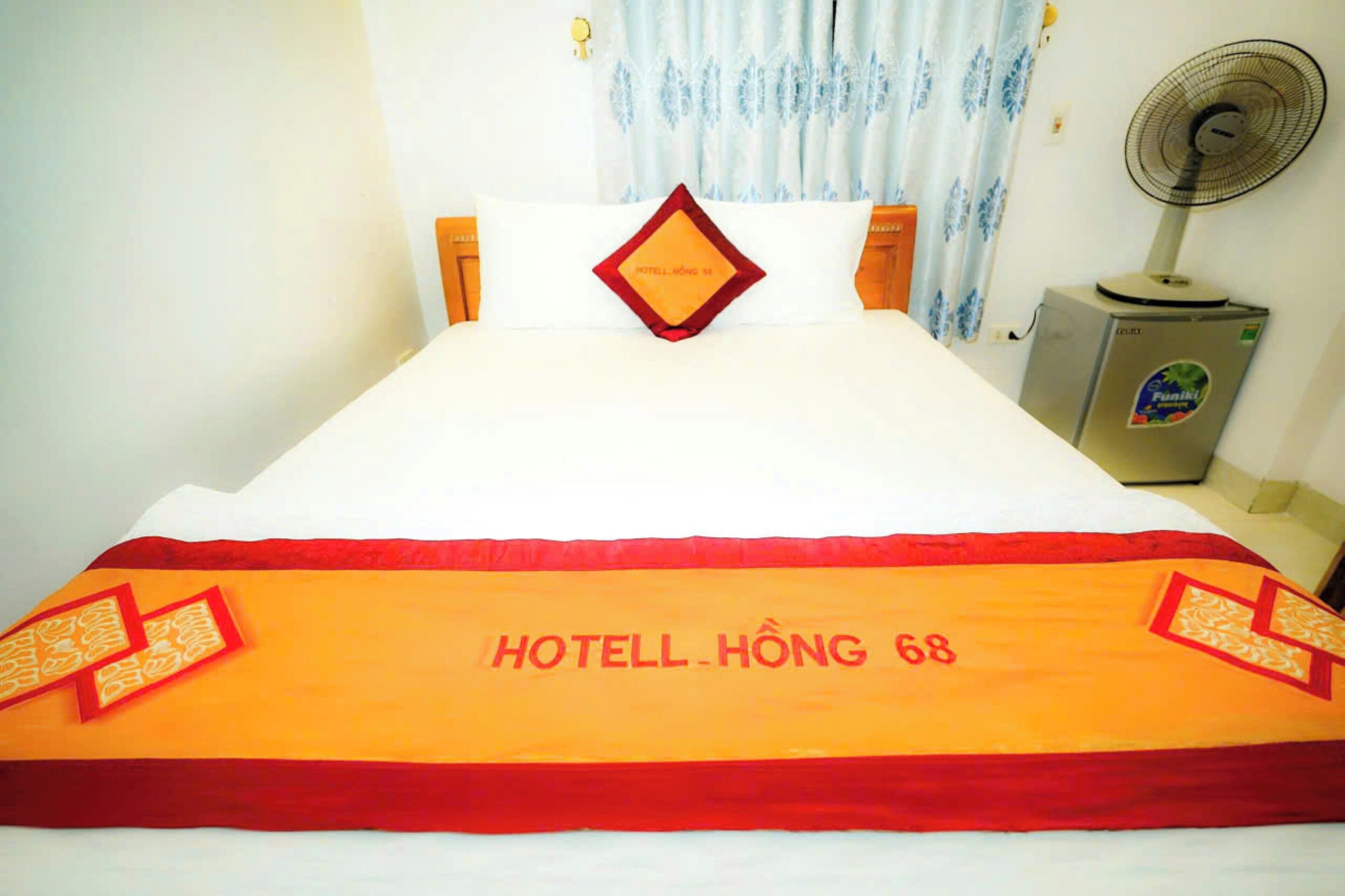A hotel room with a bed, a nightstand with a fan, and a window with curtains.