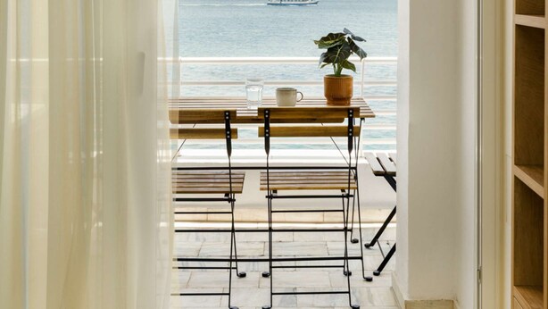Un balcone con vista sul mare, un vaso con una pianta e un tavolo con sedie.