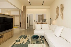 A modern living room with a flat-screen TV, a white sofa, and a glass coffee table with a decorative bowl. - Ivory by halu! - Elegant 2BD apt with sea view (Thessaloniki)