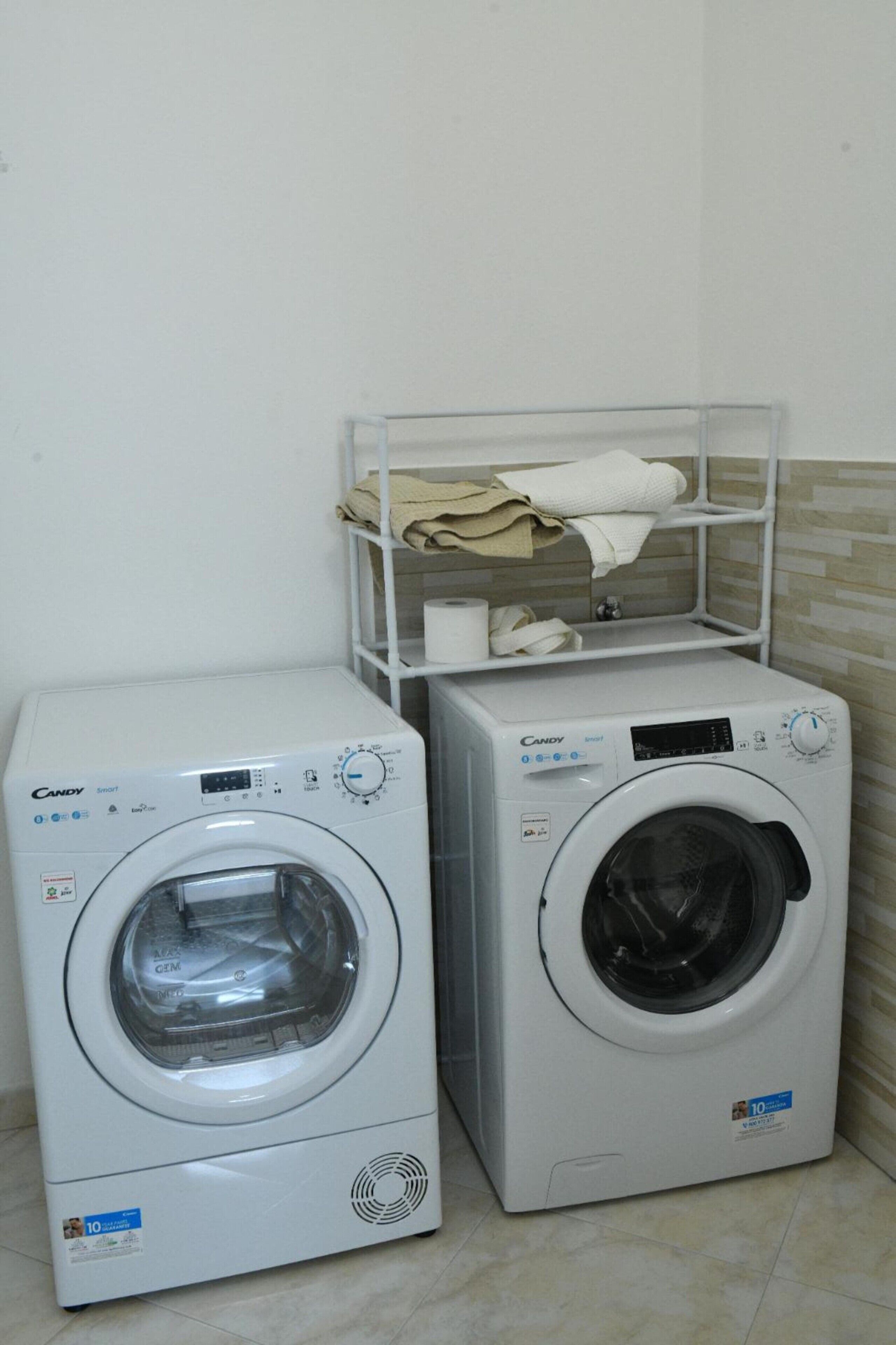 Deux lave-linge à chargement frontal de la marque Candy sont installés dans une buanderie, avec une étagère au-dessus pour ranger les serviettes.