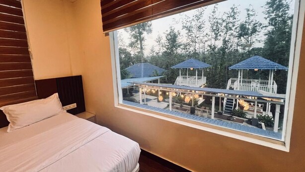 Une chambre avec une grande fenêtre donnant sur une terrasse aménagée avec des parasols et des sièges d’extérieur.