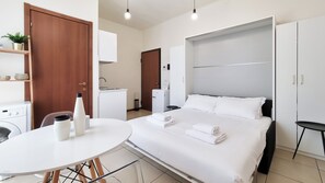 Ein modernes Hotelzimmer mit einem Bett, einem kleinen Tisch, einem Schreibtisch, einem Kleiderschrank und einer Küchenzeile.