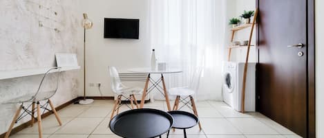 A modern kitchen with a round table, chairs, a washing machine, and a TV on the wall.