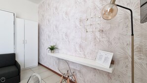 Quarto moderno com armário branco, cadeira transparente, pequena planta em vaso e prateleira fixada na parede com um documento.