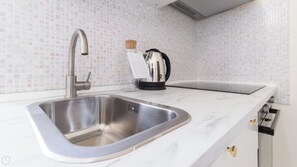 Eine Küche mit einer Edelstahlspüle, einem Wasserkocher und einer Marmorarbeitsplatte.