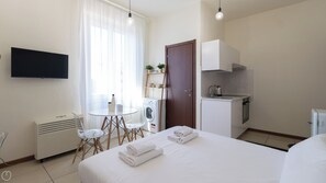A hotel room with a bed, a TV, a small kitchenette, a washing machine, and a table with chairs. - Italianway Easy - Gallura 9 (Milan)