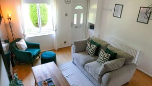 A living room with a sofa, a coffee table, a chair, a lamp, and a door with a window. - Home In Longwell Green  Inbetween Bristol and Bath (Longwell Green)