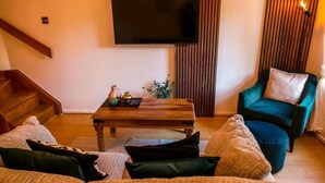 A living room with a wooden coffee table, a sofa, a teal armchair, and a flat-screen TV mounted on the wall. - Home In Longwell Green  Inbetween Bristol and Bath (Longwell Green)