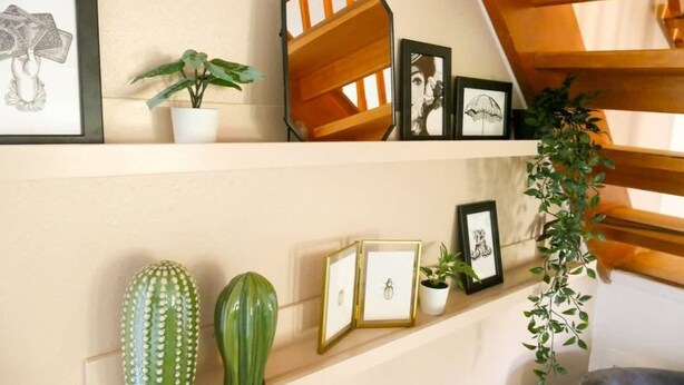 A room with a sloped ceiling, a wall-mounted shelf with framed artwork, a cactus, and a hanging plant. - Home In Longwell Green  Inbetween Bristol and Bath (Longwell Green)