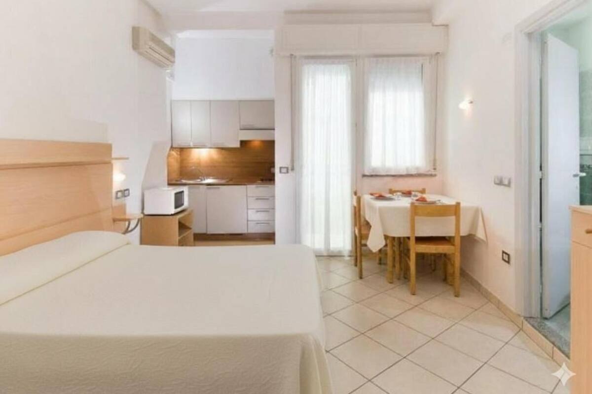 A hotel room with a bed, a small kitchenette, a dining area with a table and chairs, and a sliding glass door leading to a balcony.
