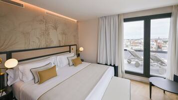 Una habitación de hotel con una cama grande, vistas de la ciudad a través de un ventanal amplio y una mesita pequeña.
