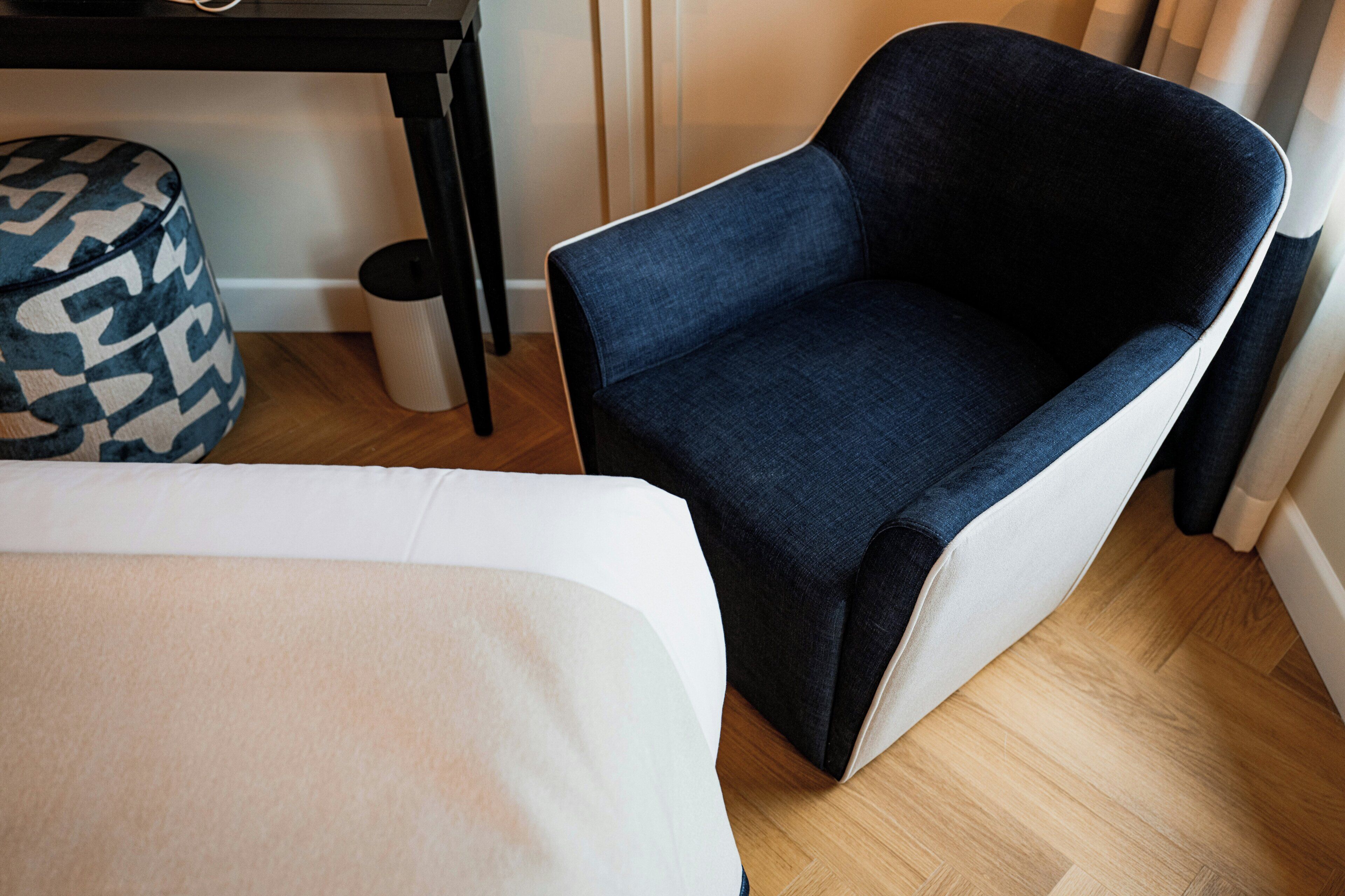 Ein modernes Zimmer mit einem dunkelblauen Sessel, einem weißen Sofa und einem gemusterten Hocker.
