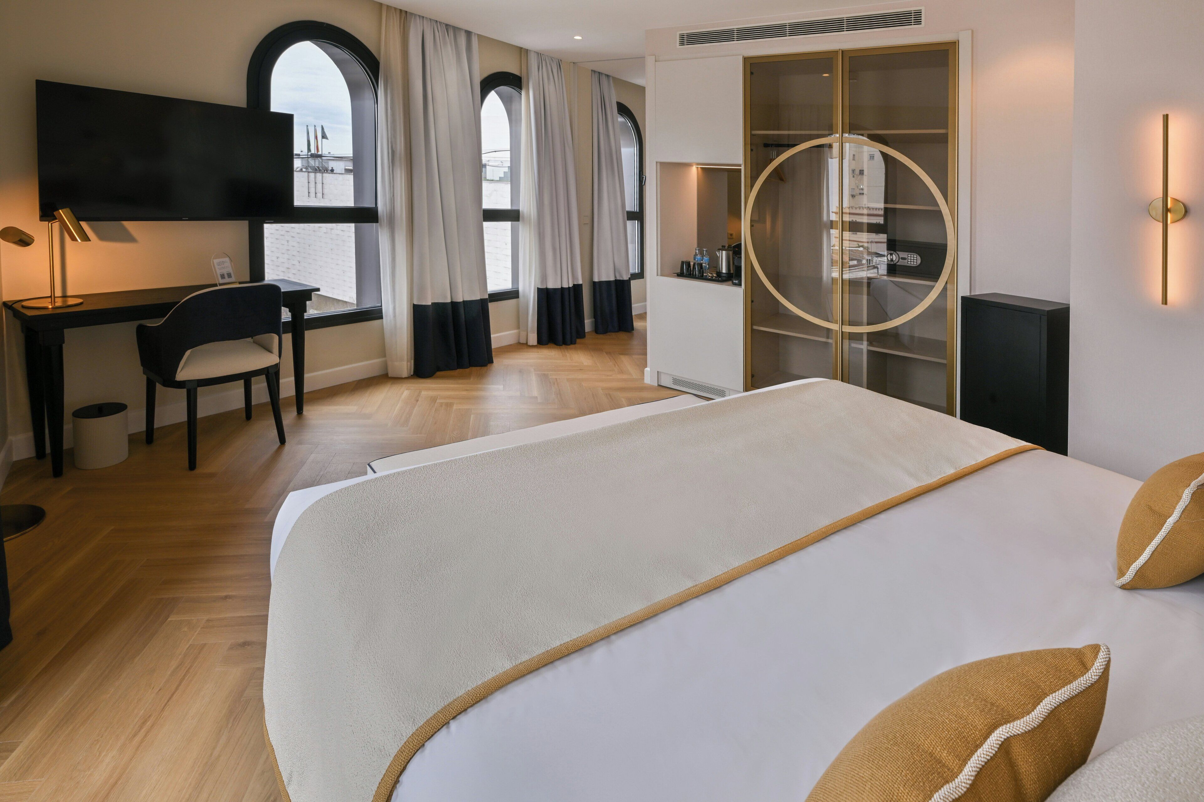 A hotel room with a bed, desk, chair, TV, wardrobe, and a view through the window.
