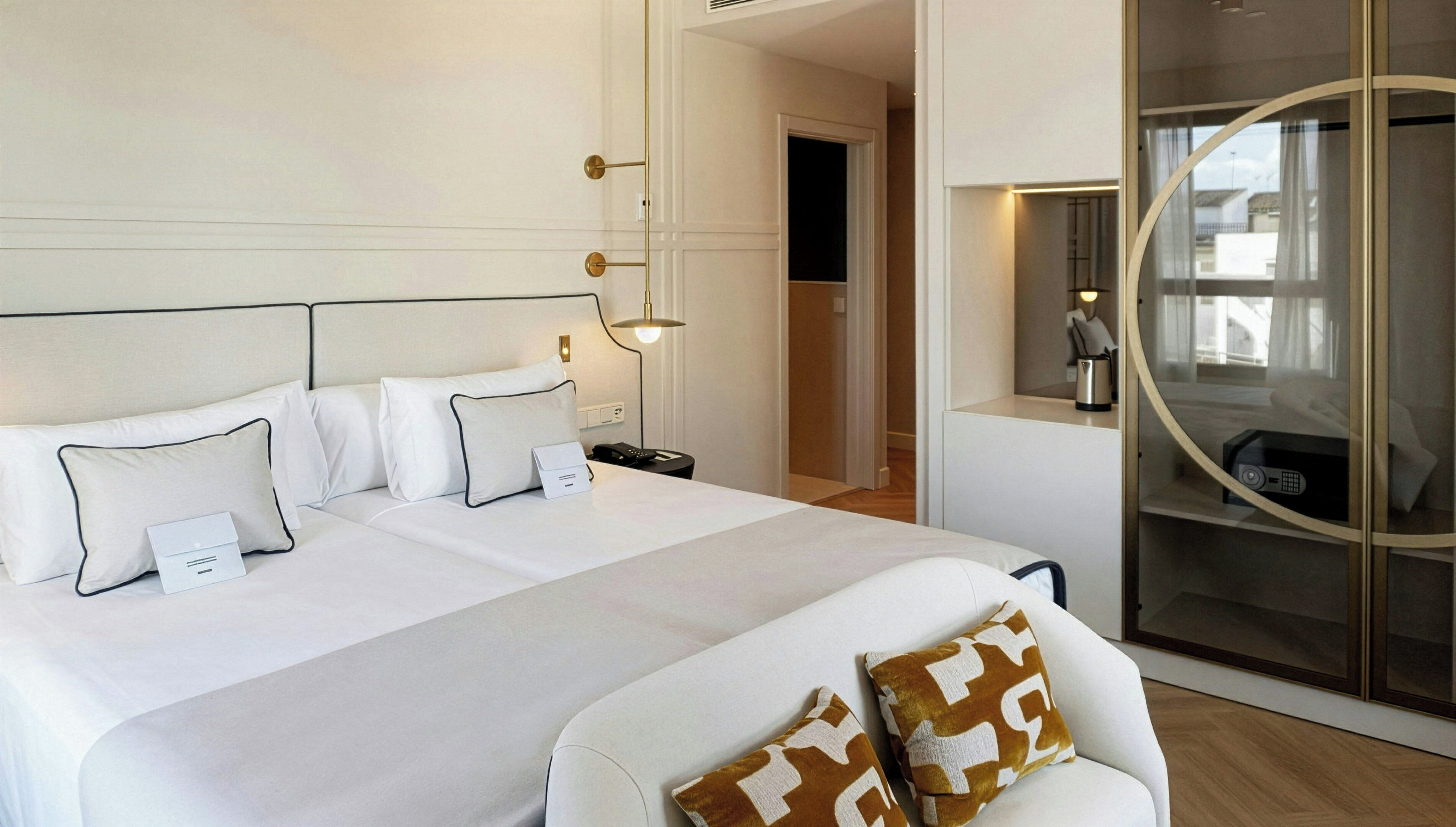 Une chambre d’hôtel avec un grand lit, des tables de chevet, une chaise et une salle de bain fermée par des parois de verre.