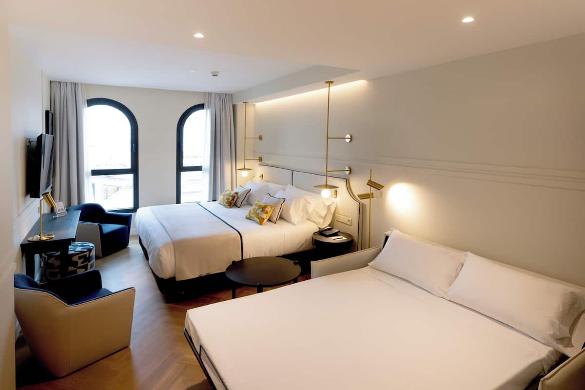 A hotel room with two beds, a desk, a chair, and a TV.