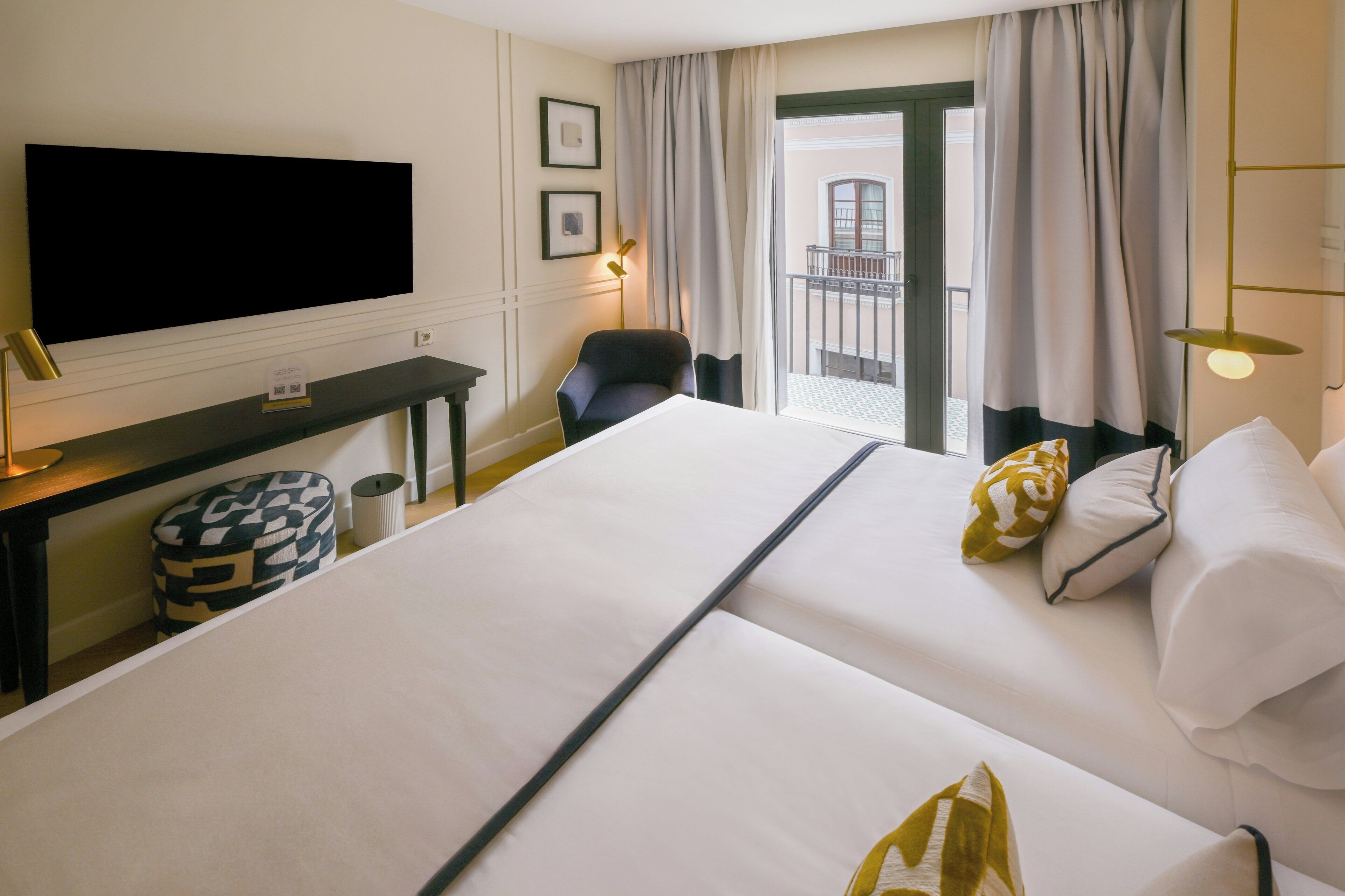 A hotel room with a large bed, a desk, a chair, a television, and a balcony view.
