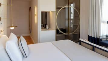 Habitación de hotel moderna con una cama grande, un vestidor y una puerta de vidrio circular.