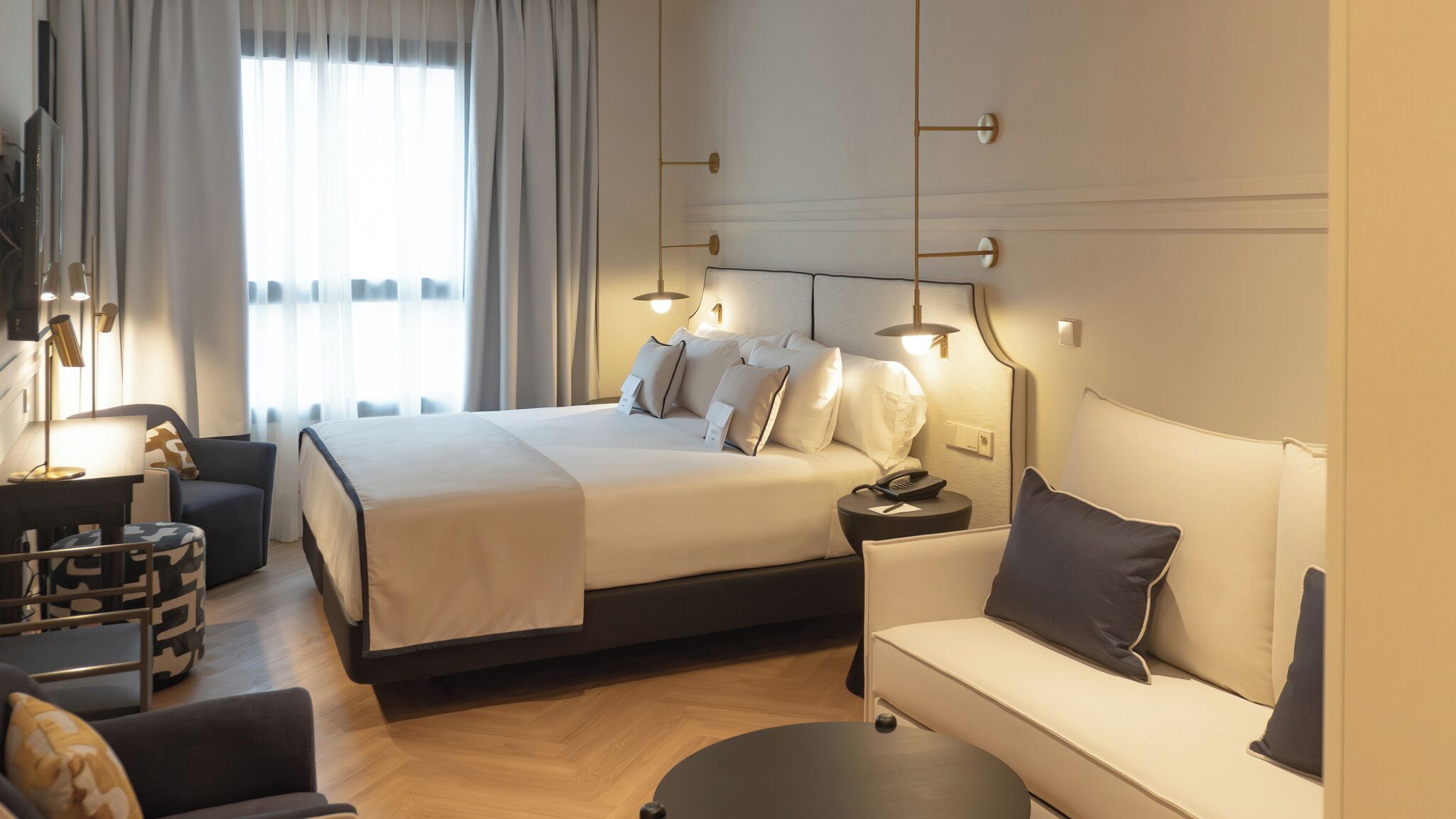 A modern hotel room with a large bed, a sofa, a desk, and a lamp.