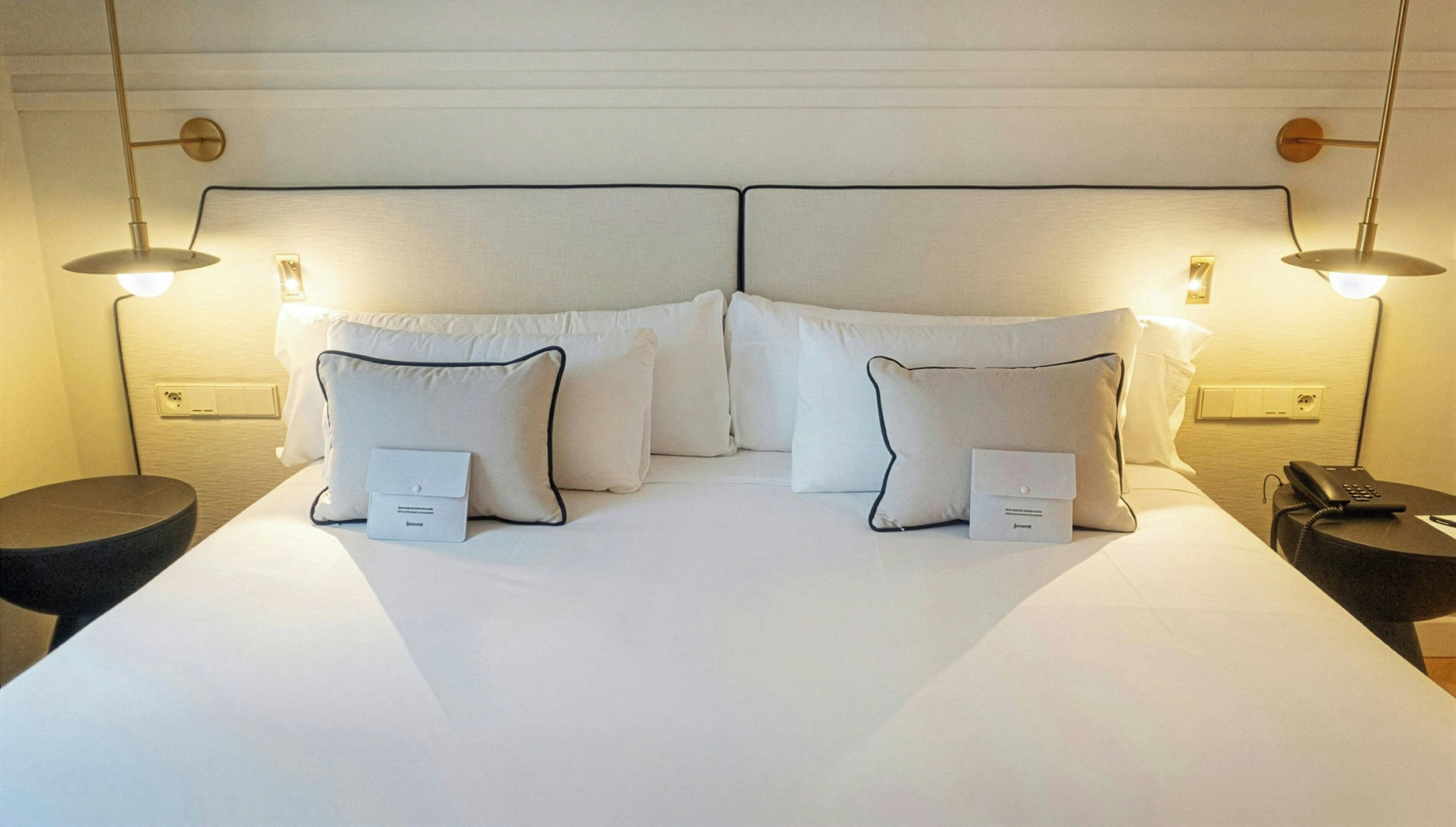 Habitación de hotel con una cama grande, dos mesitas de noche y dos lámparas de pared.
