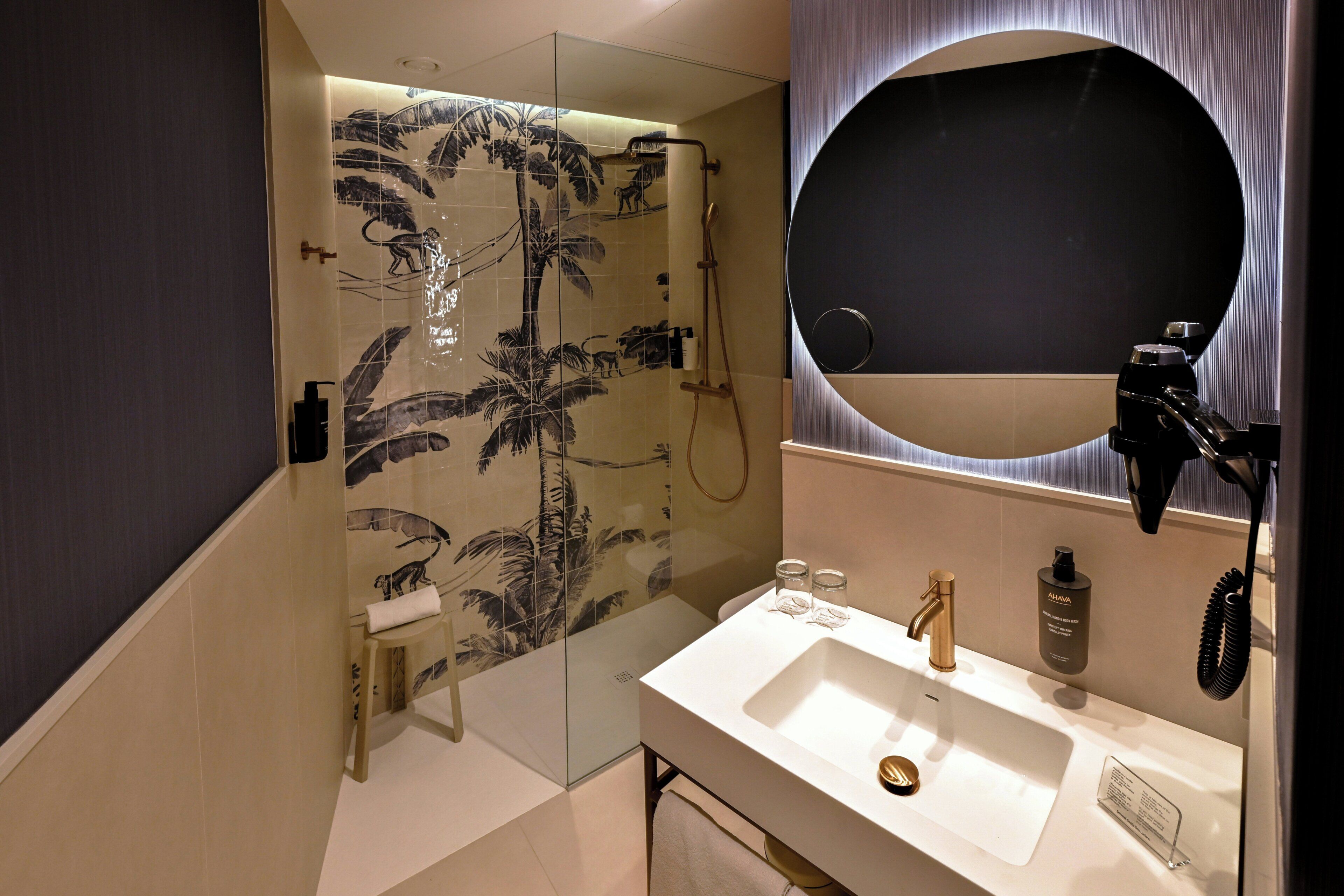 Un baño moderno con ducha envuelta en vidrio, un espejo grande y un lavabo blanco.