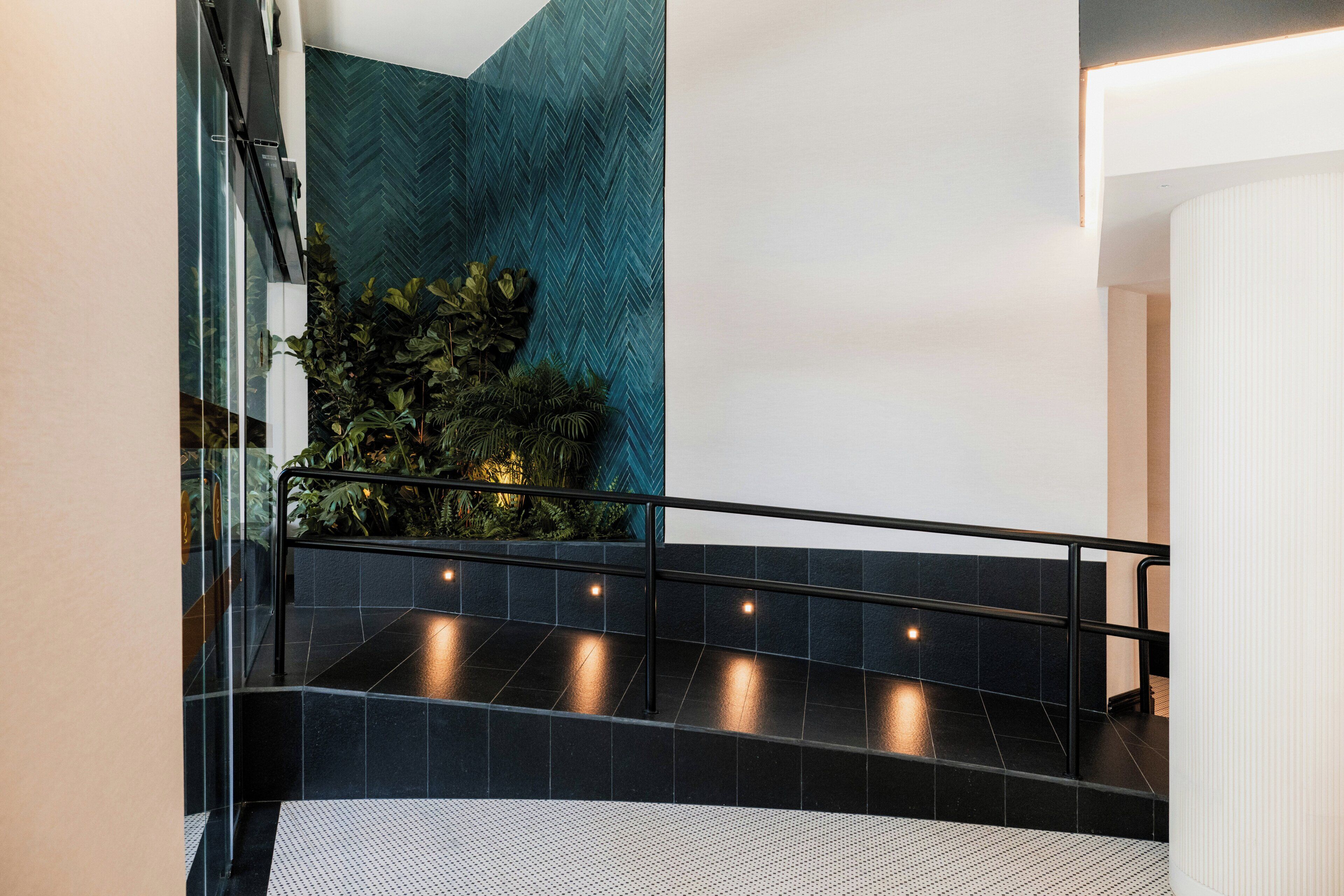 Un intérieur moderne avec un escalier, des murs recouverts de carreaux noirs et un mur vert à texture.