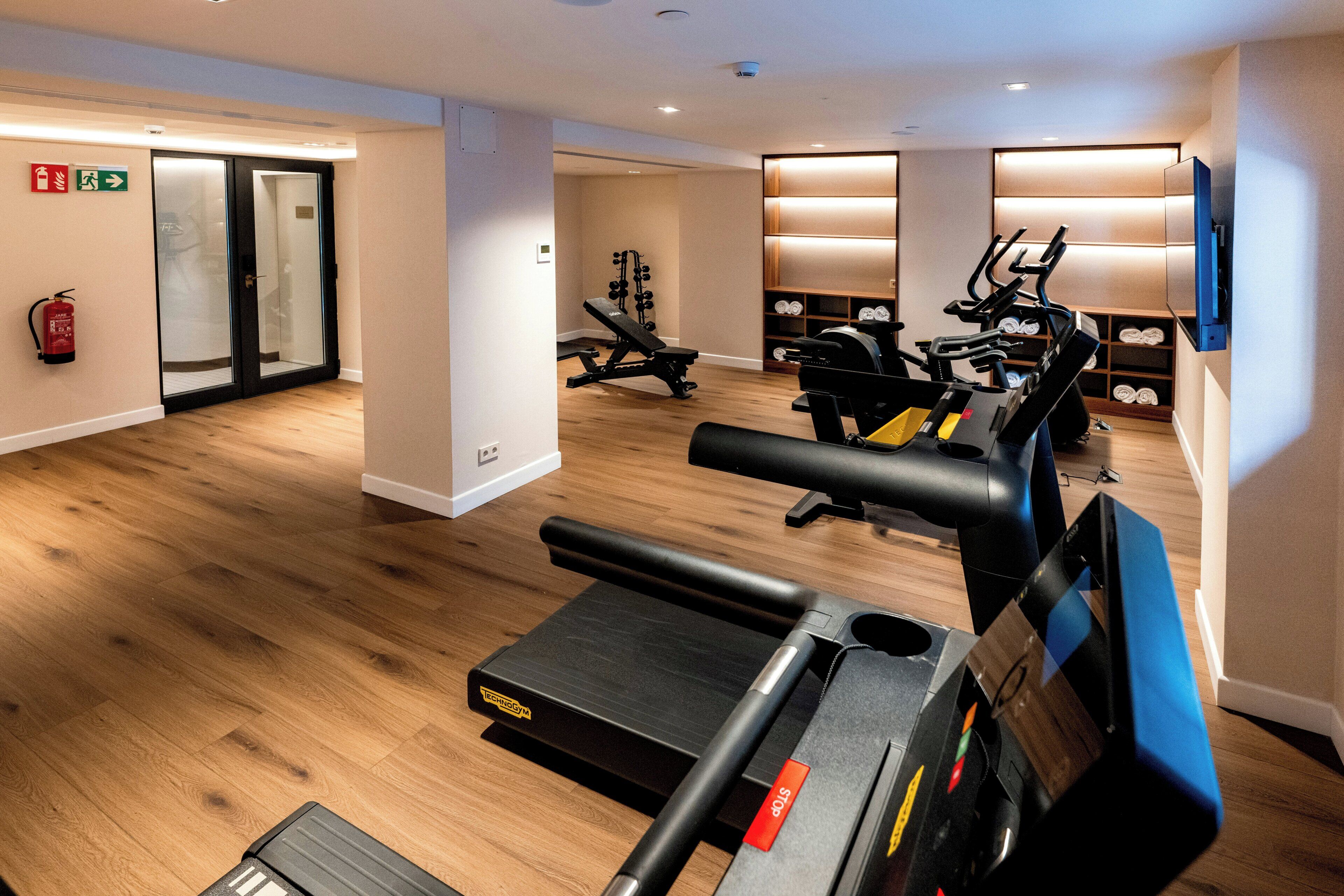 Ein Fitnessraum mit Trainingsgeräten, einem Feuerlöscher und einem Fernseher an der Wand.