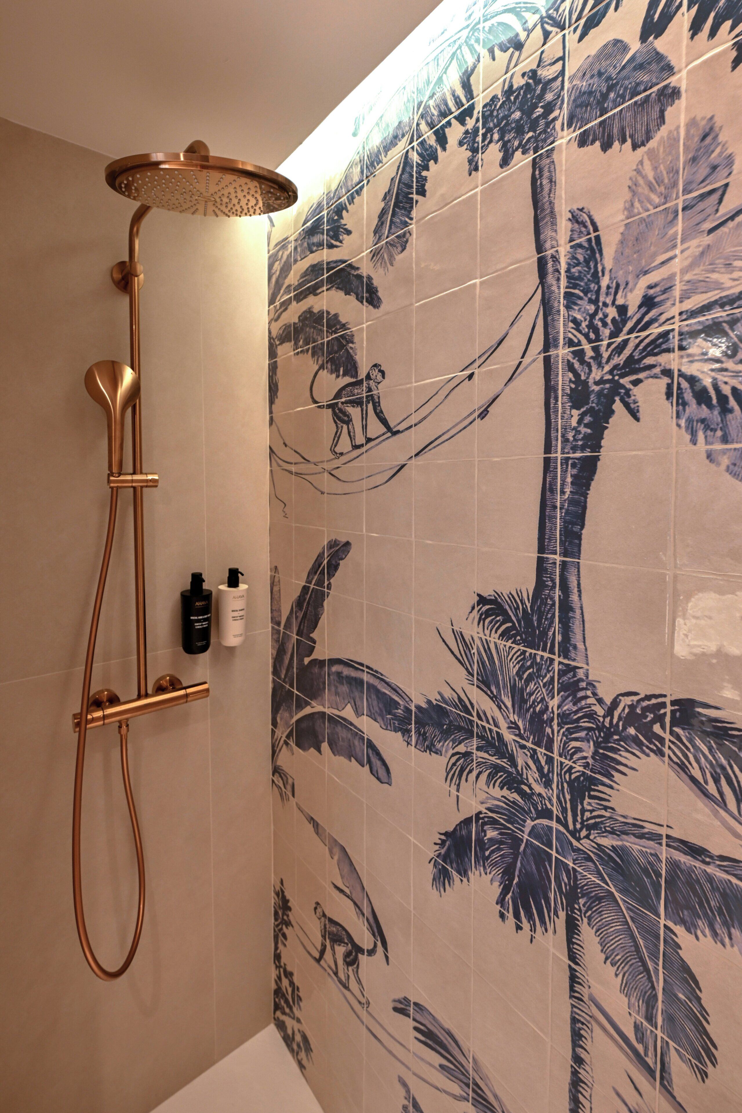 A shower with a curved head and a handheld showerhead, mounted on a wall with palm tree tiles.
