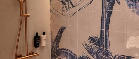 A shower with a curved head and a handheld showerhead, mounted on a wall with palm tree tiles.