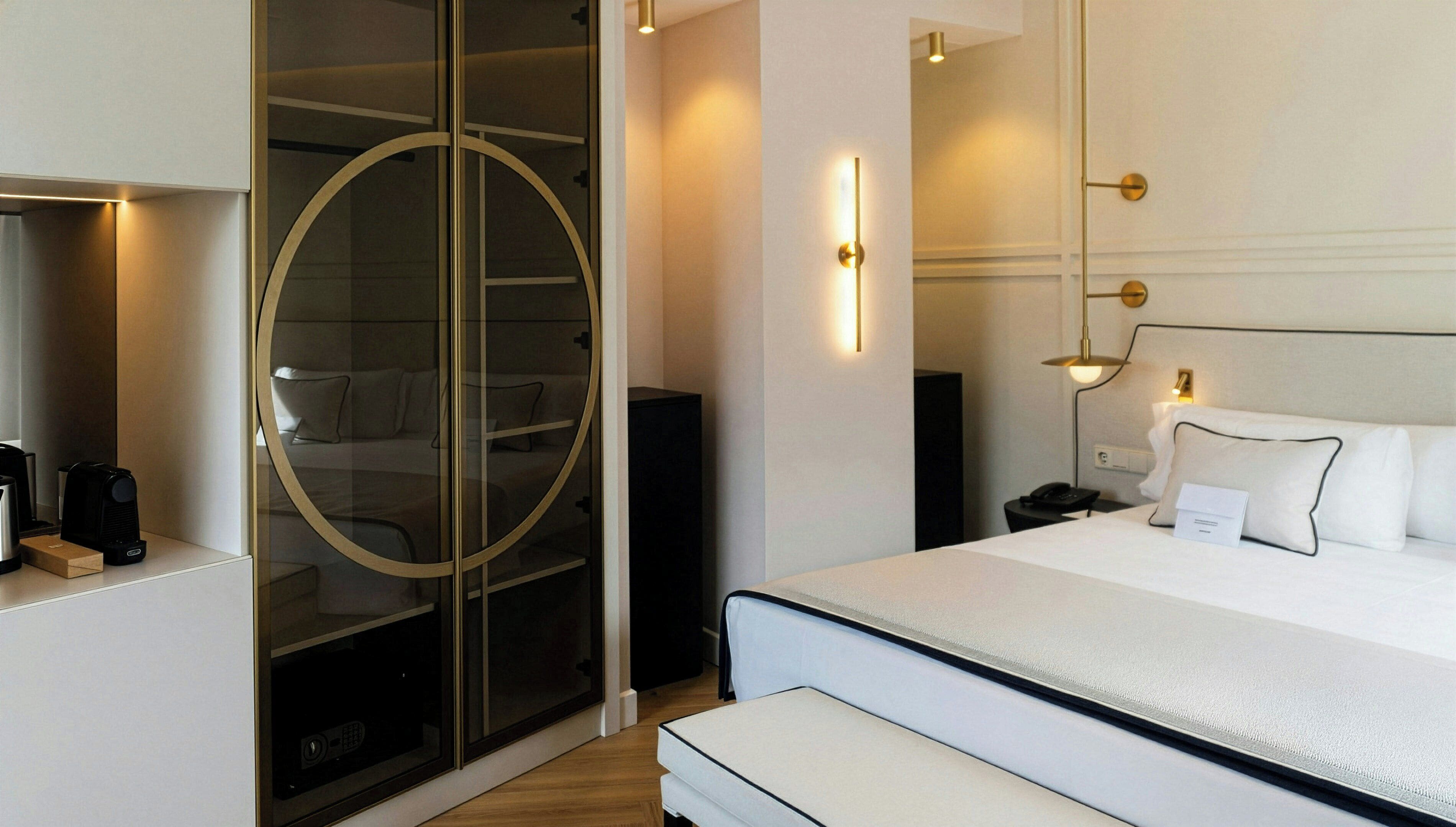 Una habitación de hotel moderna con cama, mesita de noche y puerta de vidrio circular que da a un área de ducha.