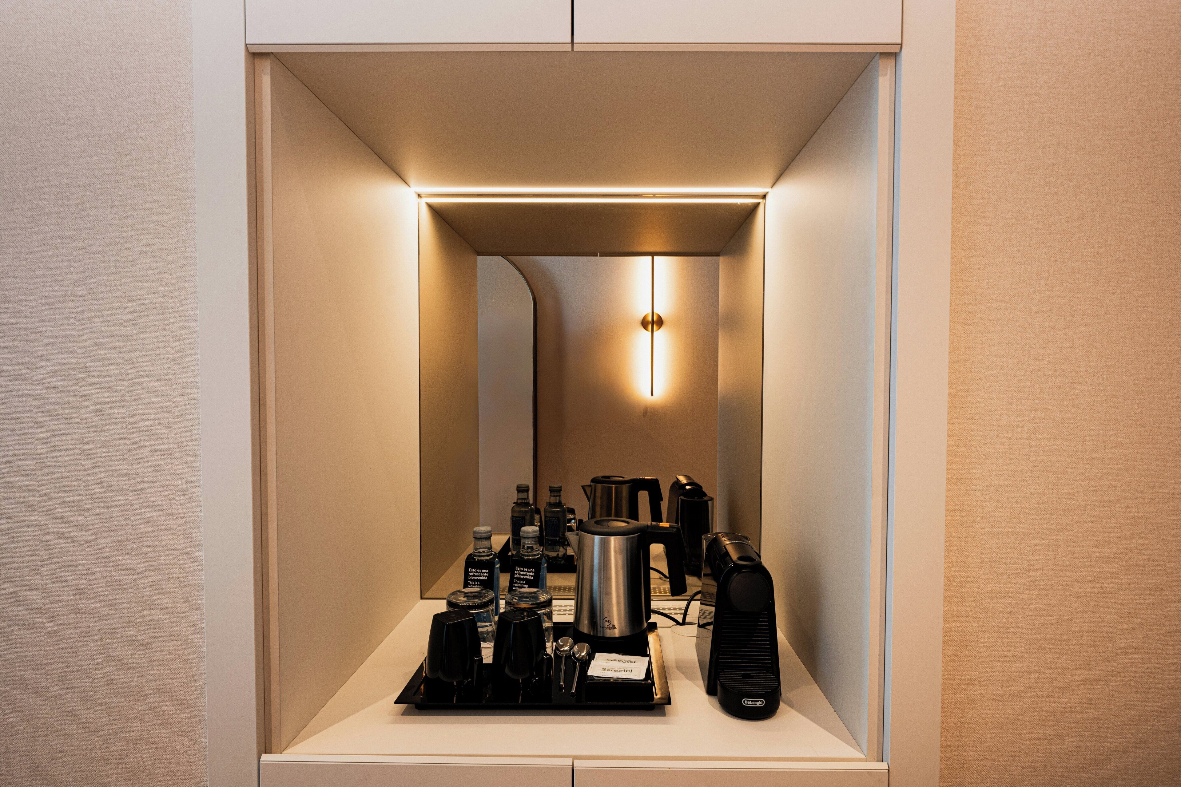 Quarto de hotel compacto com cozinha compacta, incluindo cafeteira, chaleira e outros eletrodomésticos.