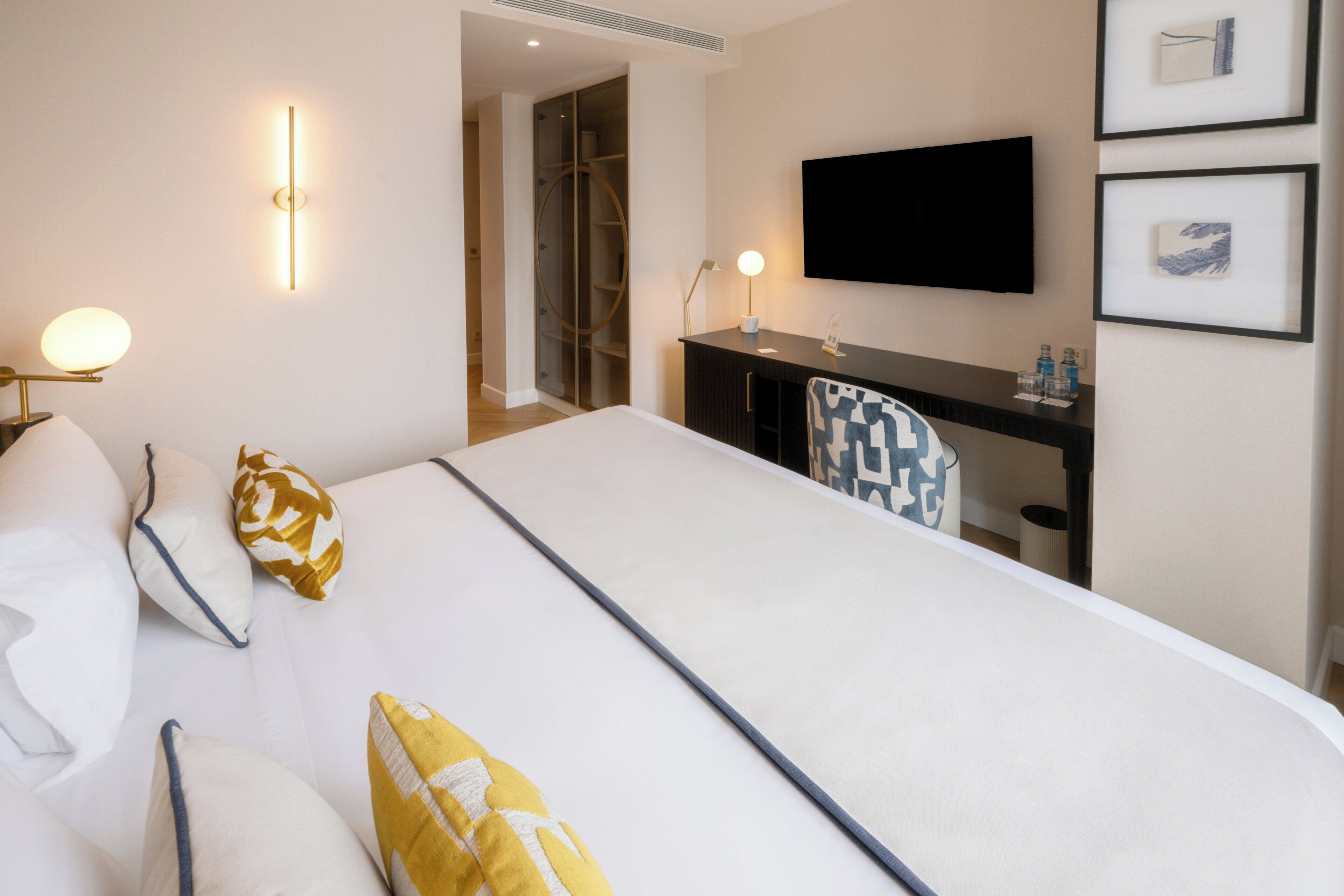 Una habitación de hotel con cama, mesita de noche, lámpara, televisión y cuadros en la pared.