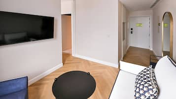 Una habitación moderna con una televisión de pantalla plana, una mesa redonda negra, un cojín estampado y una silla azul.
