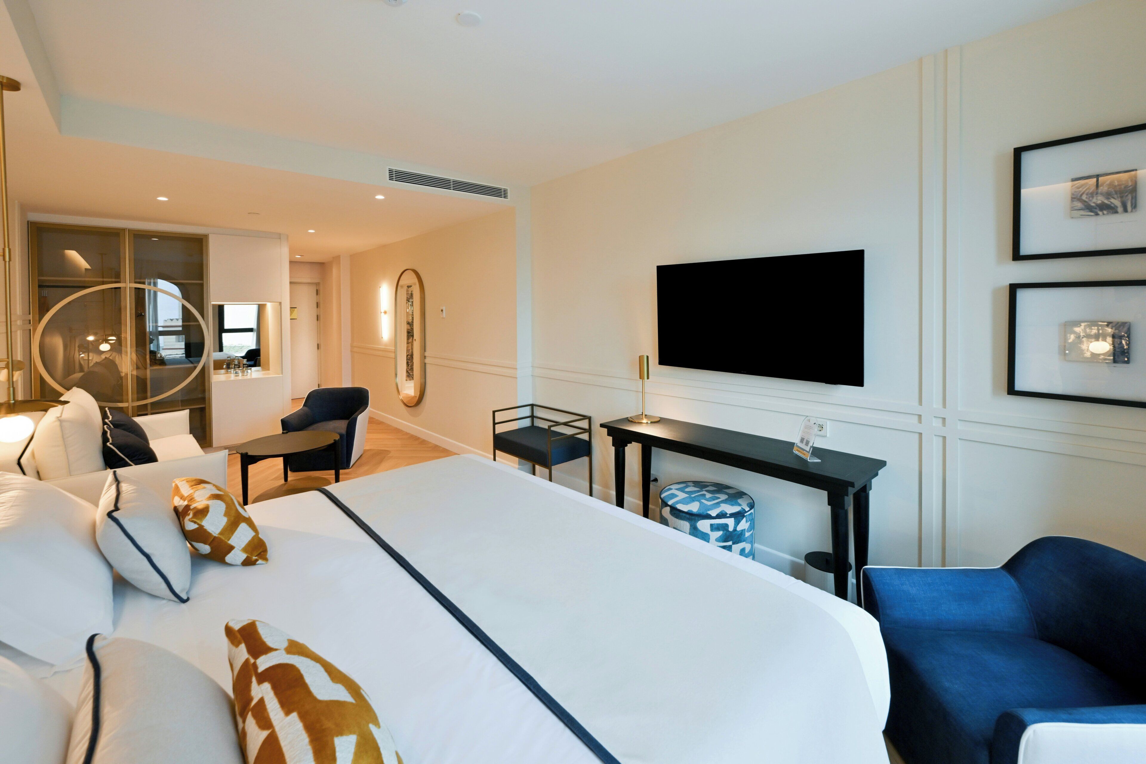 A hotel room with a large bed, a desk, a chair, a TV, and a mirror.