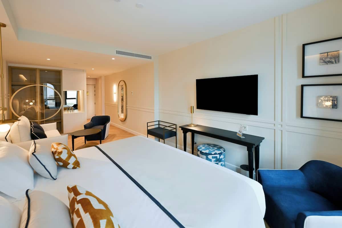 A hotel room with a large bed, a desk, a chair, a TV, and a mirror.