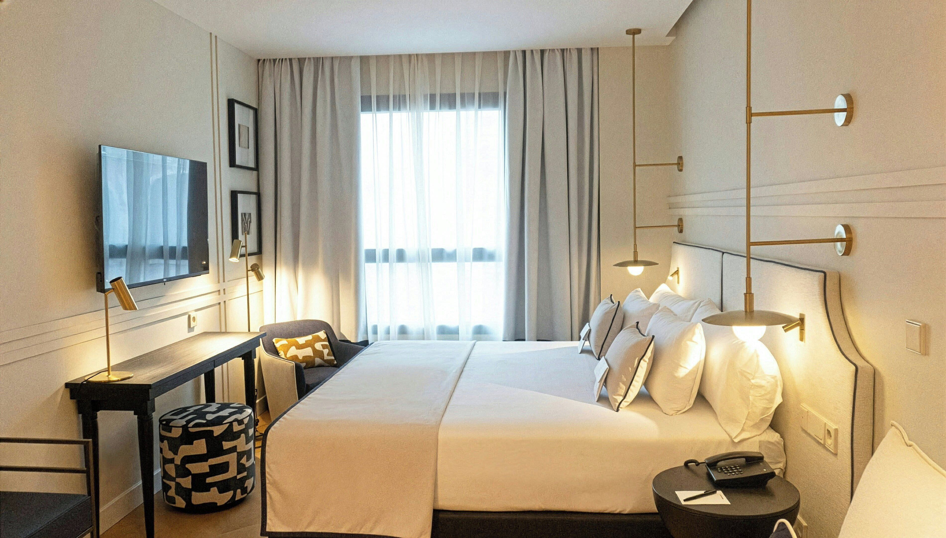 A hotel room with a large bed, bedside lamps, a desk, a chair, a television, and a window with curtains.