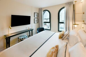 A hotel room with a bed, a desk, a chair, a TV, and two windows with curtains.