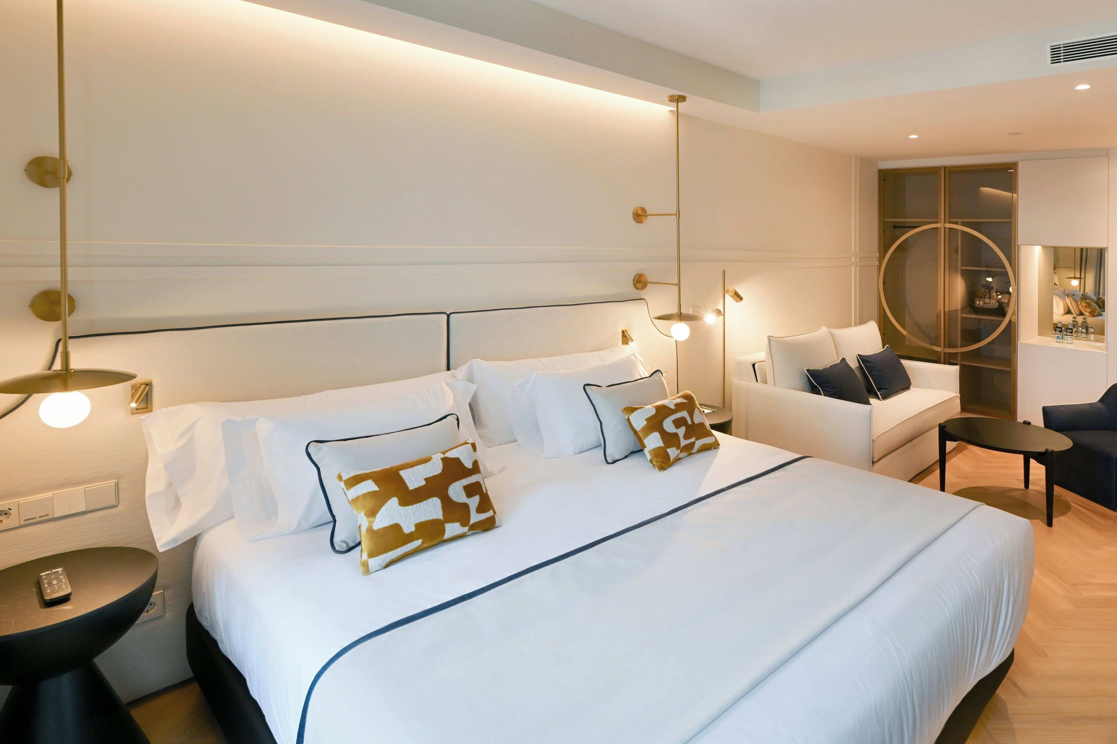 A hotel room with a large bed, bedside tables, a sofa, and a circular mirror.