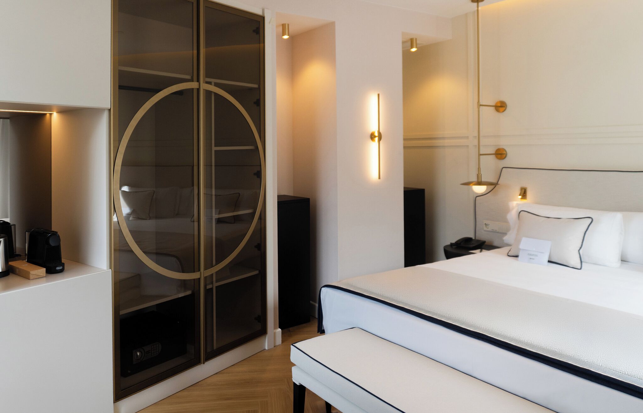 A hotel room with a bed, bedside table, and a circular glass door leading to a seating area.
