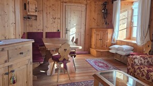 A wooden cabin interior with a dining area, a sofa, a glass-top coffee table, and a patterned rug.