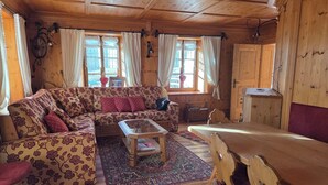 A cozy cabin interior with a wooden ceiling, a sofa set, a coffee table, and a dining table.