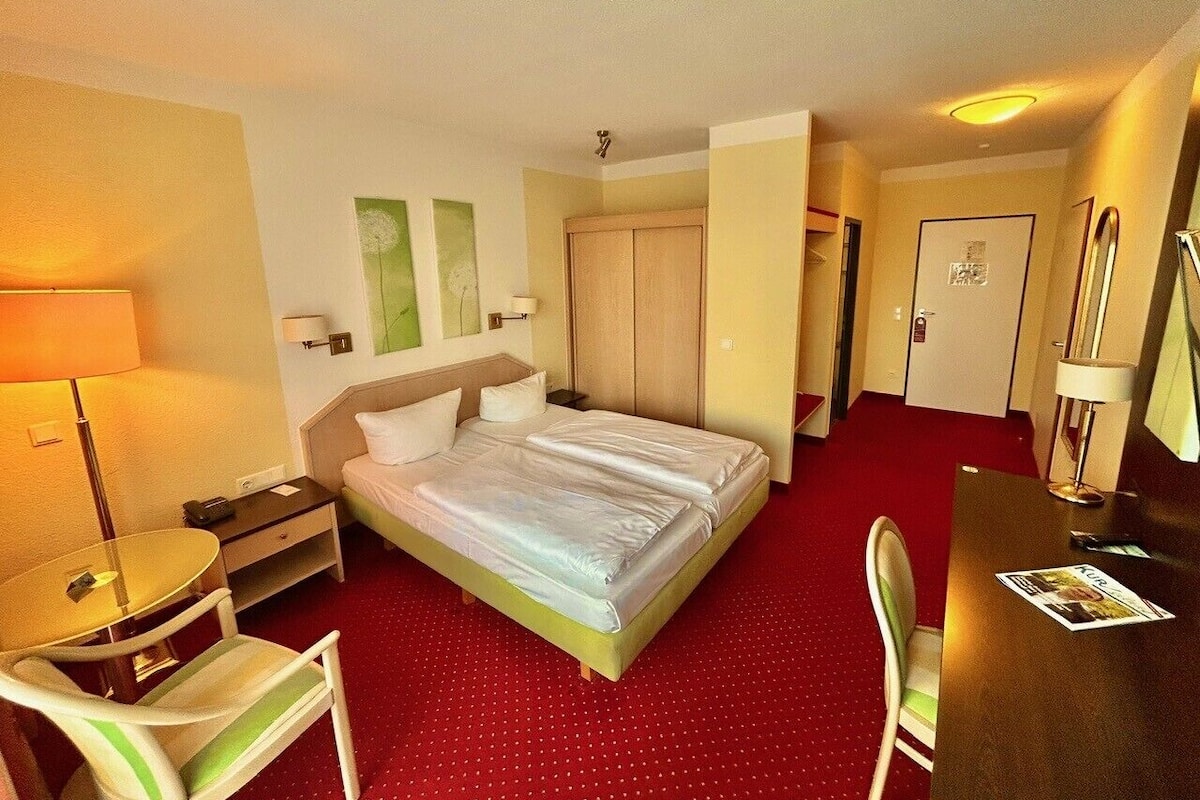 Ein Hotelzimmer mit Bett, Schreibtisch, Stuhl, Lampe und Tür.