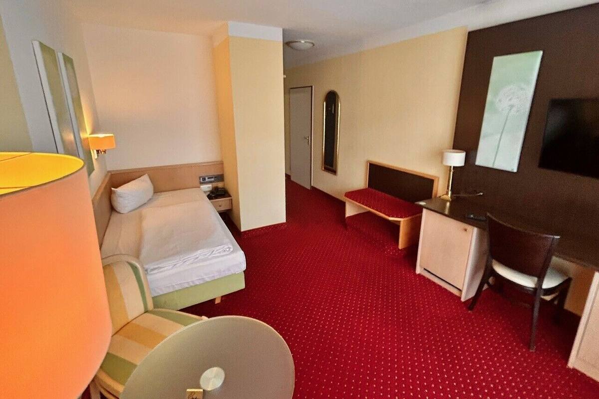 Ein Hotelzimmer mit Bett, Schreibtisch, Stuhl, Nachttisch, Lampe und Spiegel.