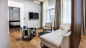 Una camera d'albergo moderna con divano, due poltrone, un tavolino, una televisione e una finestra con tende.